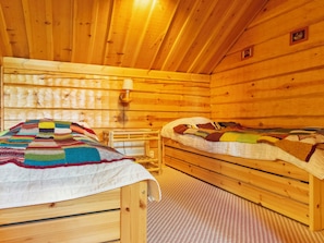 Una baita in legno con due letti di legno, una coperta all'uncinetto e un tavolino.