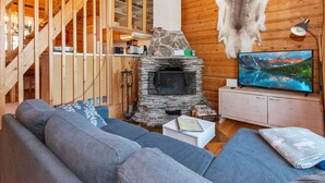 A cozy cabin interior with a stone fireplace, wooden walls, a sofa, and a television.