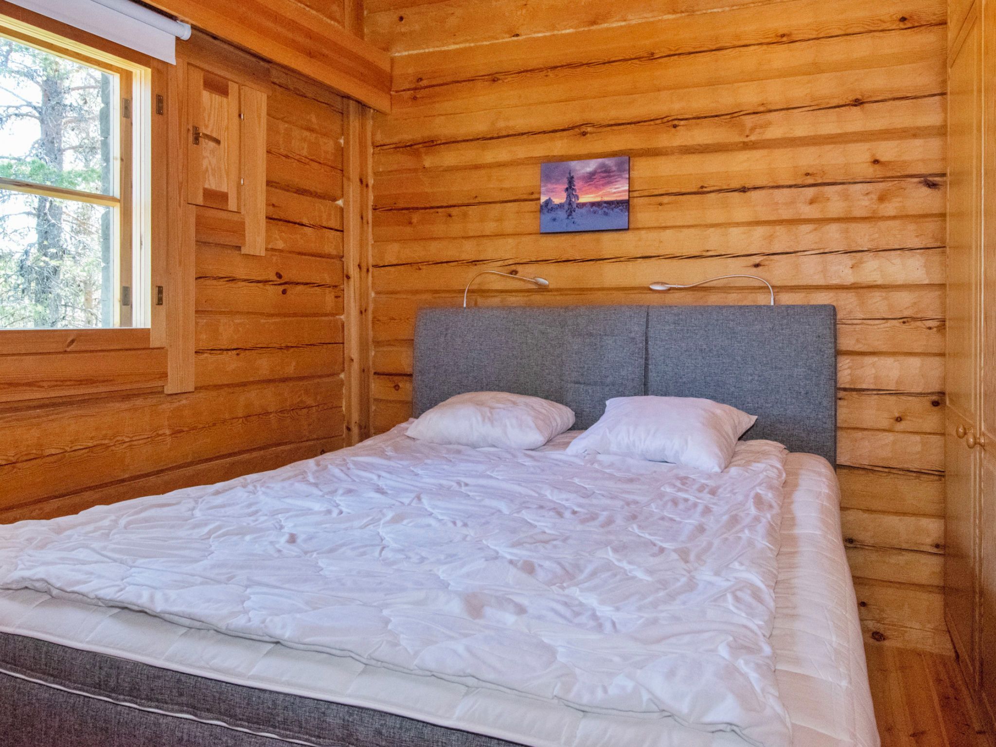 A wooden cabin bedroom with a bed, a window, and a painting on the wall.