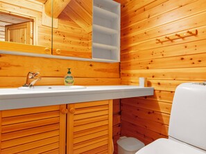 Baño de cabaña de madera con lavamanos blanco, espejo y retrete.