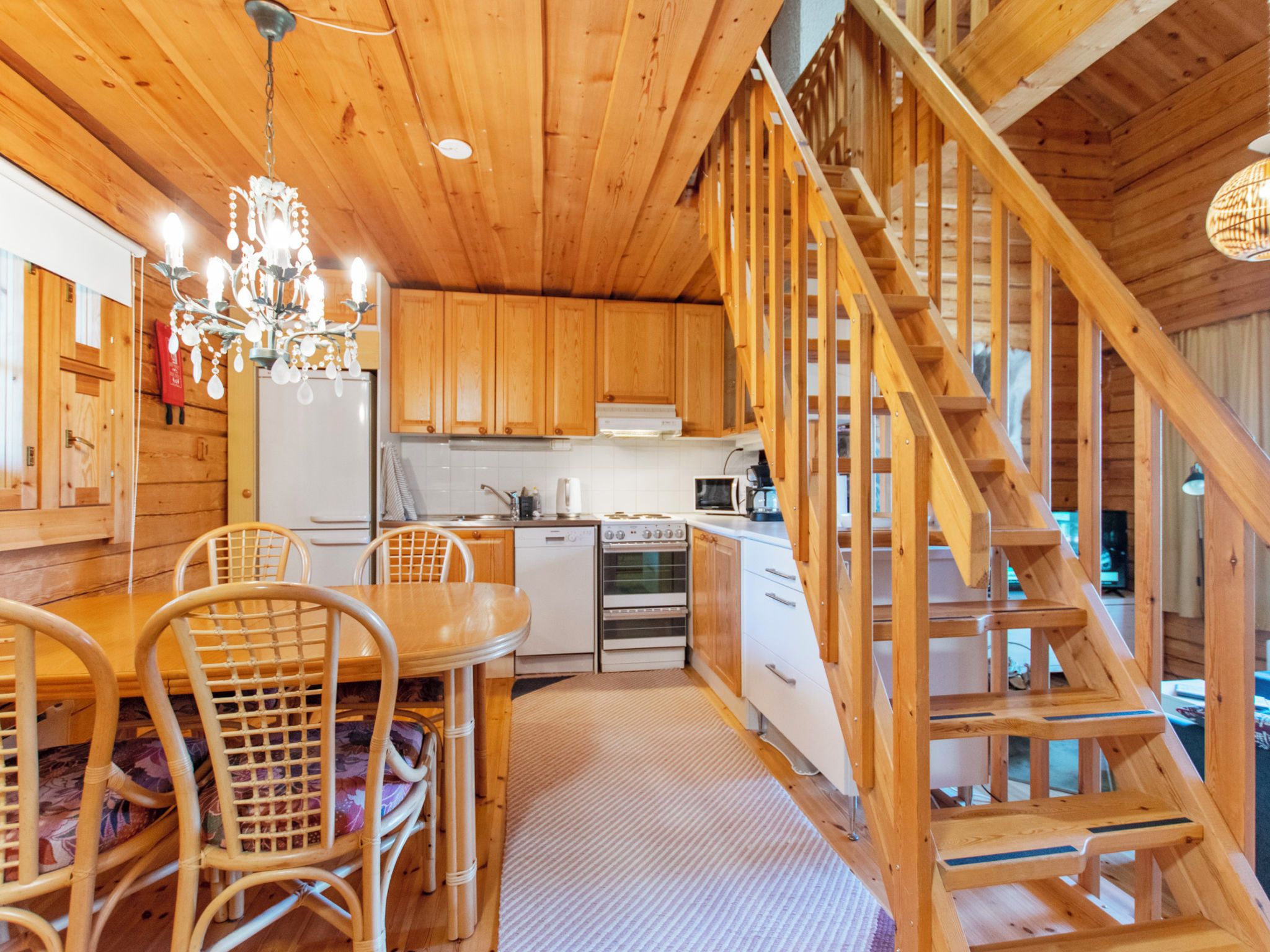 A wooden interior with a kitchen, dining area, and a wooden staircase.