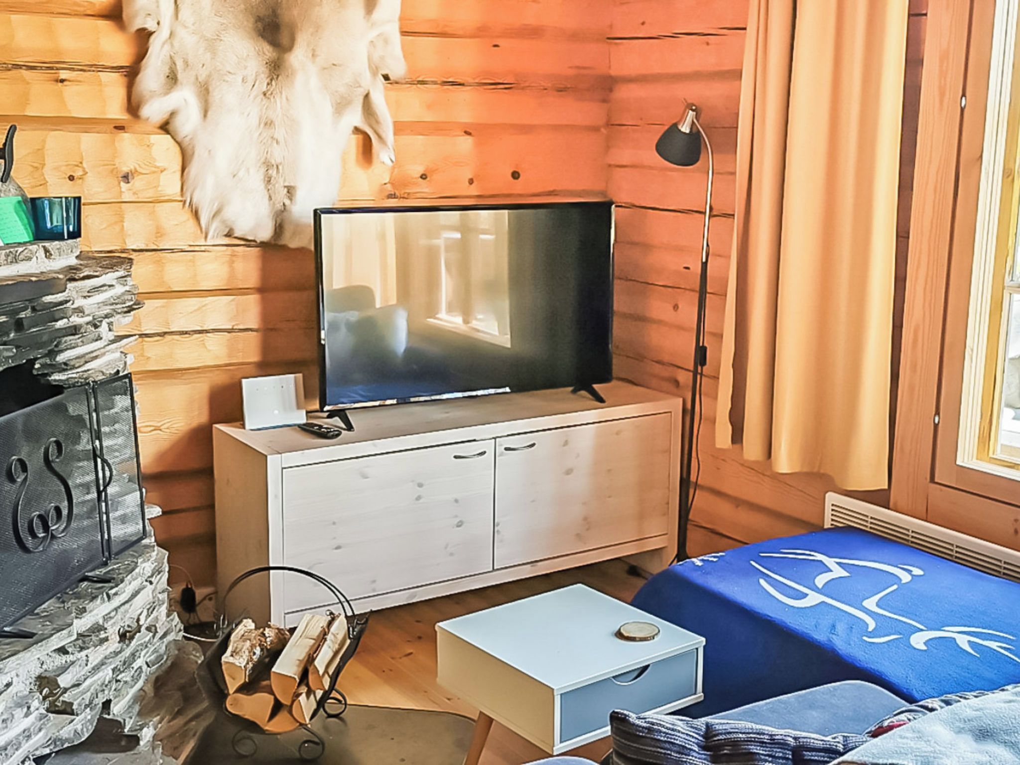 L’intérieur d’une cabane avec une télévision posée sur un meuble en bois, une cheminée et un lit recouvert d’une couverture bleue.