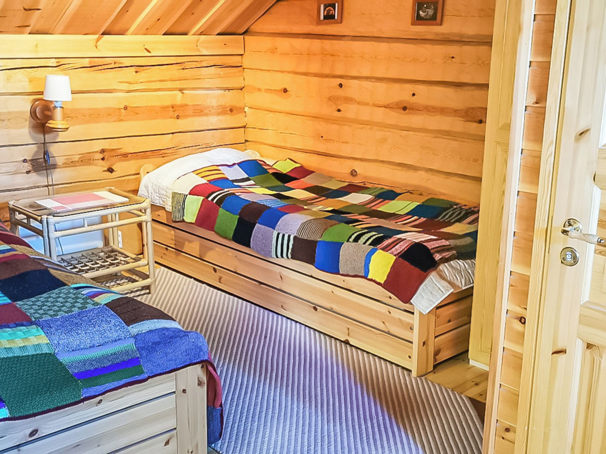 Een slaapkamer in een houten blokhut met een enkel bed, een nachtkastje, een lamp en een gestreept vloerkleed.