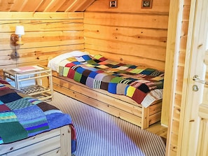 Une chambre dans une cabane en bois, avec un lit simple, une table de chevet, une lampe et un tapis à rayures.