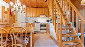 A wooden cabin interior with a kitchen, dining area, and a wooden staircase.