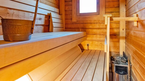 A wooden sauna with benches, a window, and a metal bucket.