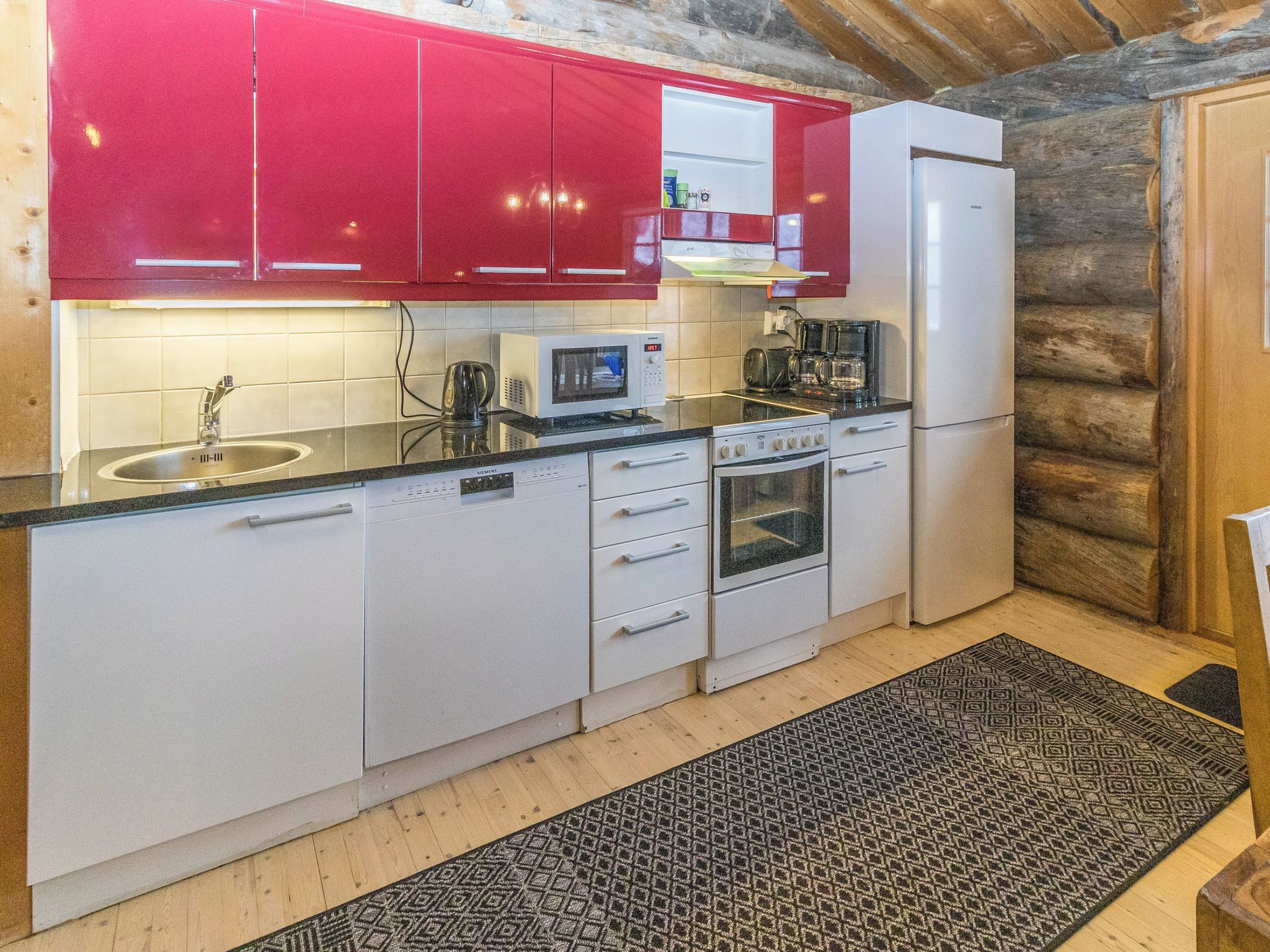 Una cocina con armarios superiores rojos, un refrigerador blanco, un microondas Siemens, una cafetera y una estufa.