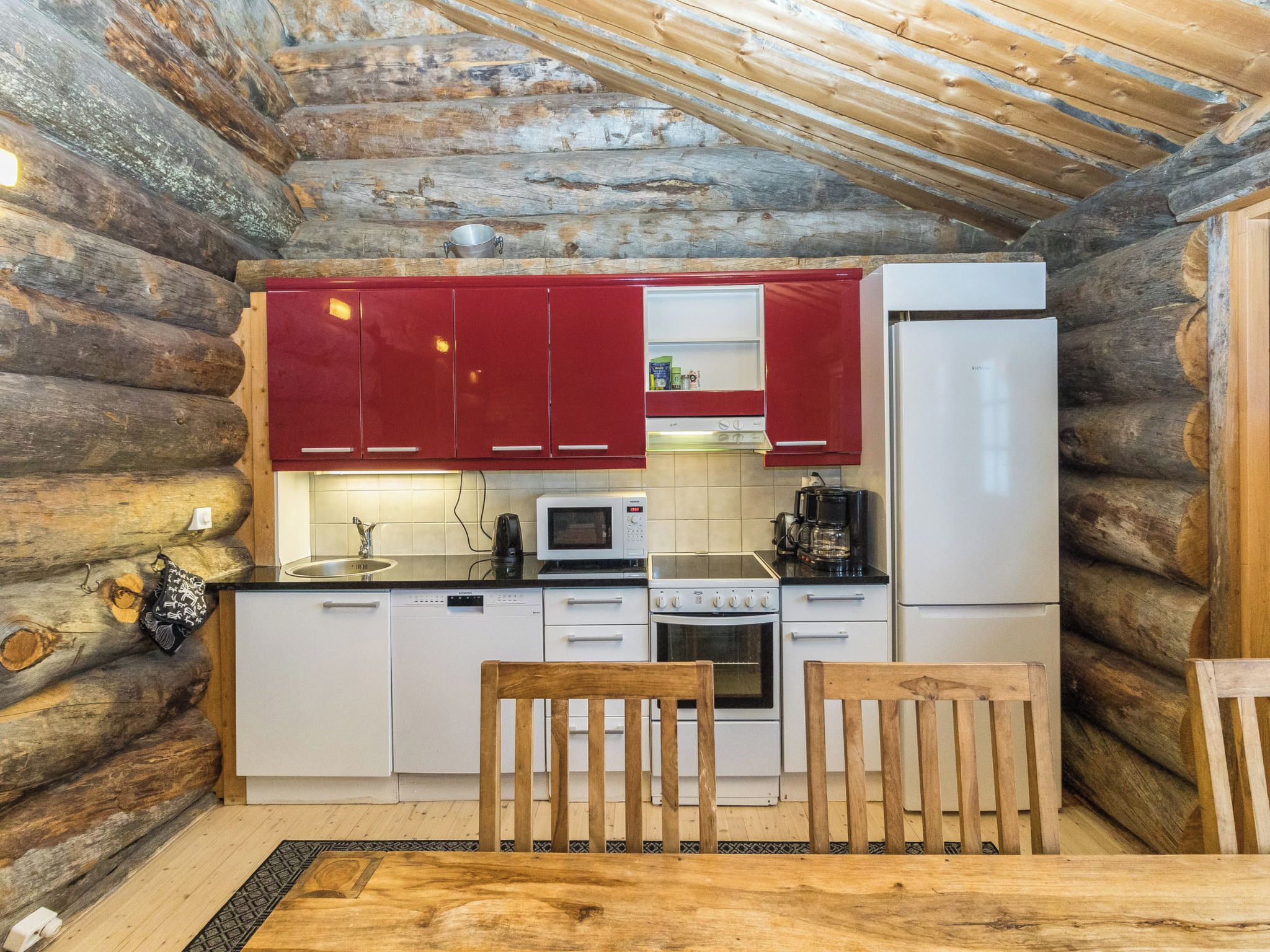 A compact kitchen with wooden walls, a wooden table, and basic appliances including a microwave, stove, and refrigerator.