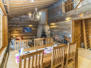 A cozy log cabin interior with a stone fireplace, wooden furniture, and a dining area.