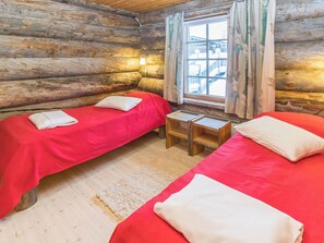 A log cabin room with two beds, a small table, and a window with curtains. - Apartment Talles by Interhome (Inari)