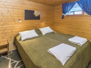 A wooden cabin room with a bed, two wall-mounted lamps, and a window with curtains.