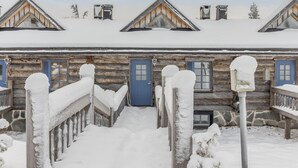 Una cabaña de troncos con una entrada cubierta de nieve y múltiples ventanas.