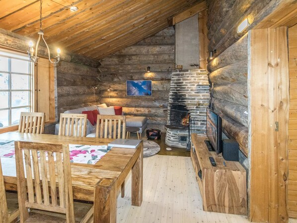 Cozy cabin interior with a dining table, sofa, stone fireplace, and large window.