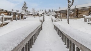 Un sendero de madera cubierto de nieve que lleva a cabañas de troncos, también con nieve en los tejados y árboles.
