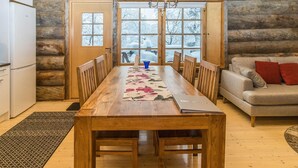 Una mesa de comedor de madera con sillas, un sofá y un refrigerador en el interior de una cabaña de troncos.
