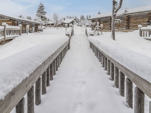 A snow-covered wooden pathway leading to a row of log cabins.