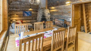 Un acogedor interior de cabaña de troncos con chimenea de piedra, mobiliario de madera y una mesa de comedor.