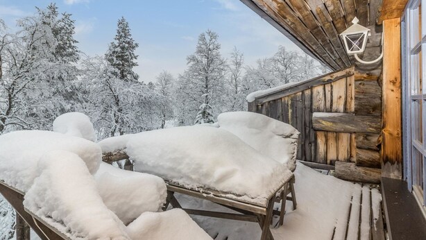 Una cabaña de madera con un porche cubierto de nieve y bancos.