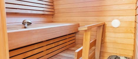 Una sauna con bancos de madera, un recipiente metálico y una ventana.