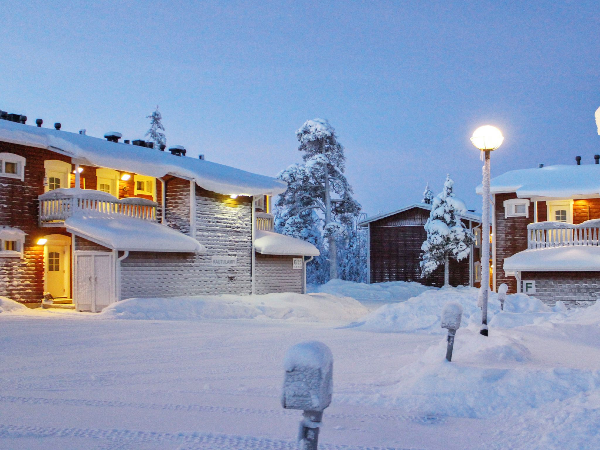 A snow-covered residential area with houses, a street lamp, and a mailbox.