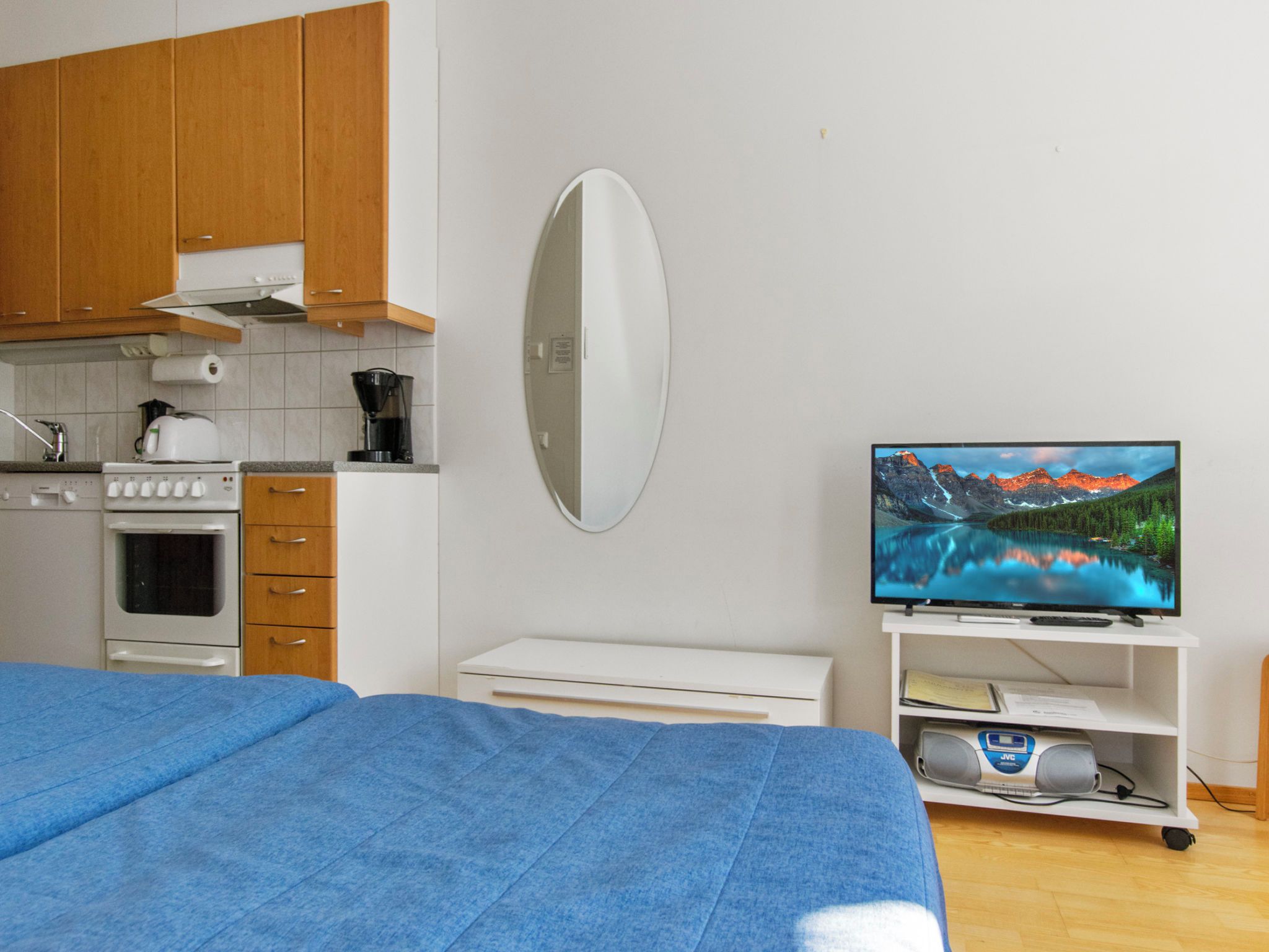 A bedroom with a bed, a TV, a kitchenette, and a bathroom.