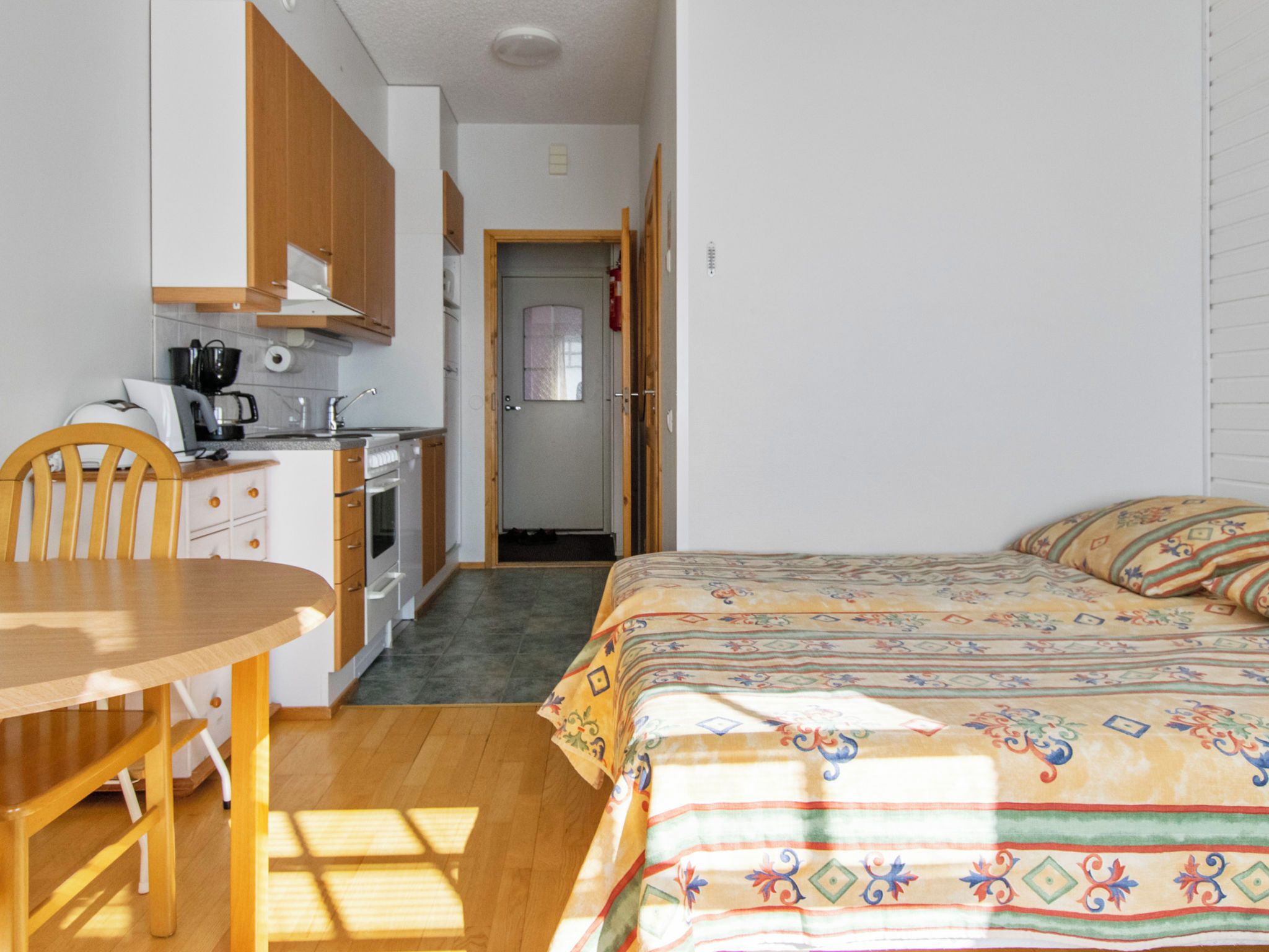 A compact room with a bed, a small kitchenette, and a wooden chair.
