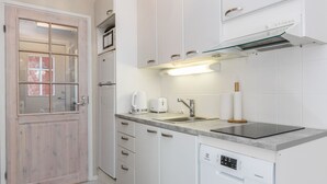 Una cocina moderna con armarios blancos, lavavajillas empotrado, tostadora y pileta de acero inoxidable.