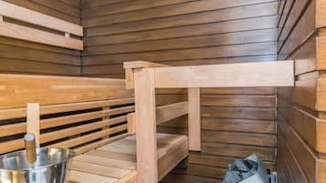 A sauna with wooden benches, a metal bucket, and a trash bin.