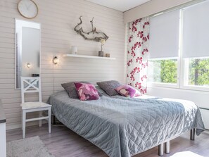 A bedroom with a bed, a nightstand, a mirror, a wall-mounted clock, a decorative piece, and a window with curtains. - Moitakuru a17 by Interhome (Inari)