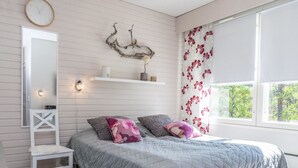 Un dormitorio con una cama, una mesita de noche, un espejo, un estante en la pared y una ventana con cortinas.