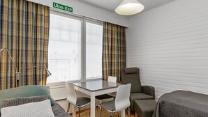 Ein Zimmer mit einem Bett, einem Schreibtisch, zwei Stühlen, einem Tisch und einer Lampe. Über der Tür befindet sich ein Schild mit der Aufschrift 'Ulos-Exit'.