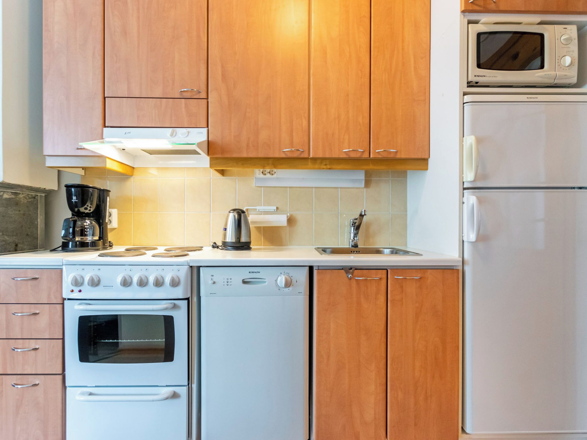 Een keuken met houten kastjes, een fornuis, een vaatwasser, een magnetron en een koffiezetapparaat.