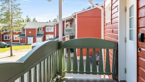 A wooden porch with a green railing, a red building in the background, and a clear sky.