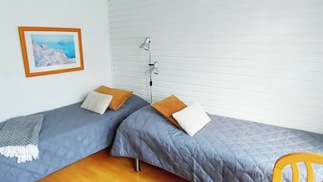 Een kamer met twee eenpersoonsbedden, een staande lamp, een ingelijste foto aan de muur en een houten vloer.