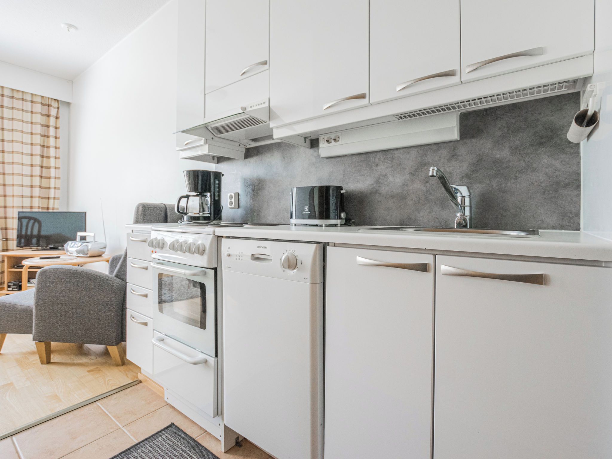 Une cuisine moderne avec des meubles blancs, un four encastré, un lave-vaisselle, une machine à café et un grille-pain.
