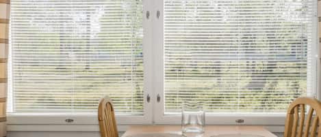 Una habitación con una mesa redonda de madera, dos sillas y una ventana con persianas.