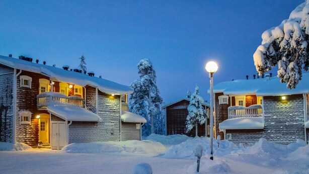 A snow-covered building with a balcony, a garage, and a snow-covered tree.