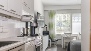 A modern kitchen with white cabinets, a coffee maker, and a stove. There is a dining area with a table and chairs, and a window with blinds.