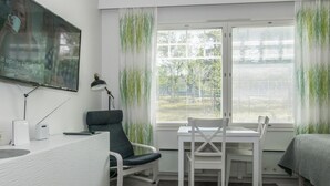 A modern room with a desk, two chairs, a bed, a TV, and a window with blinds.