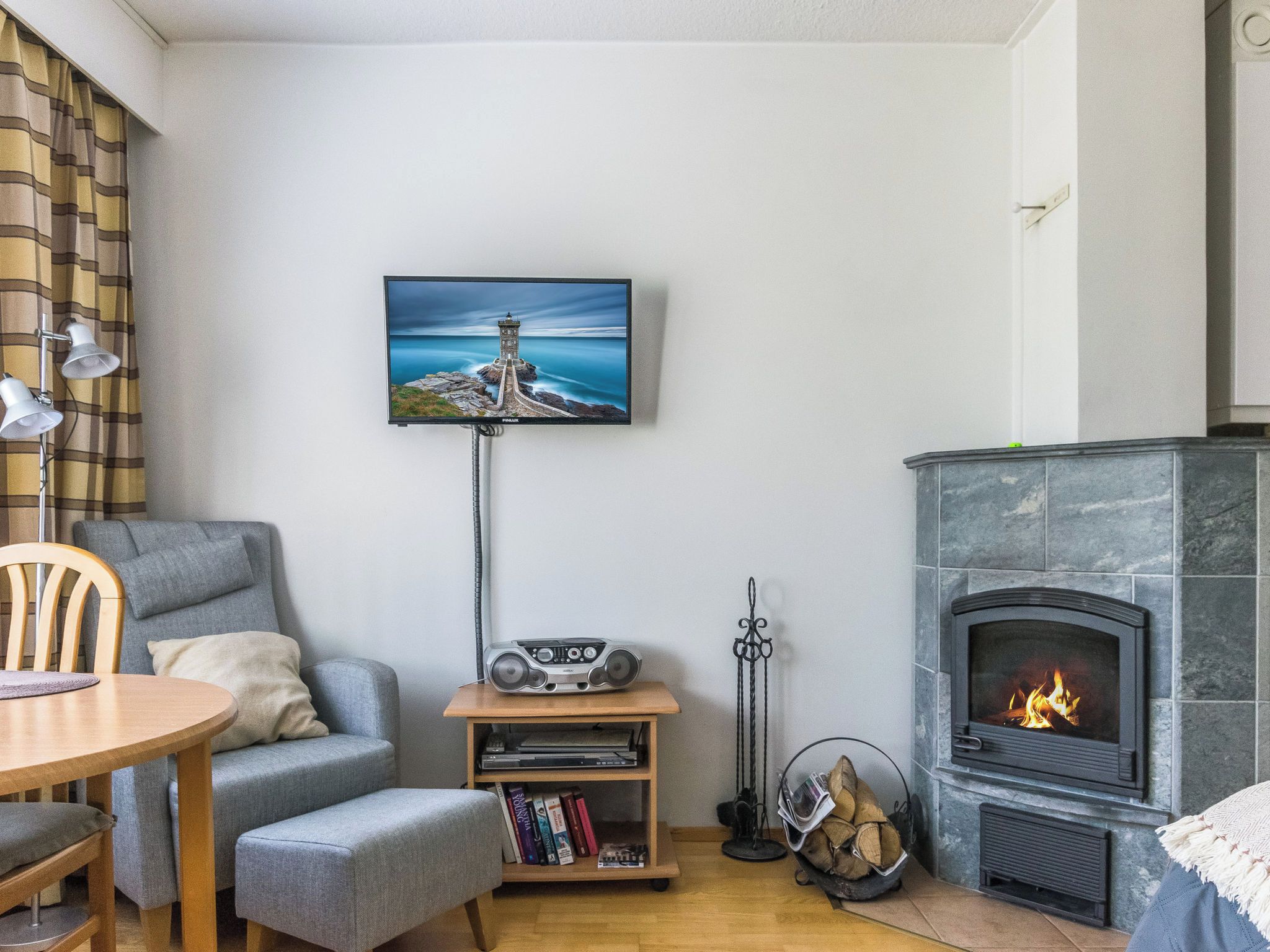 Een gezellige woonkamer met een open haard, een aan de muur bevestigde televisie, een bank, een tafel en een boekenplank.