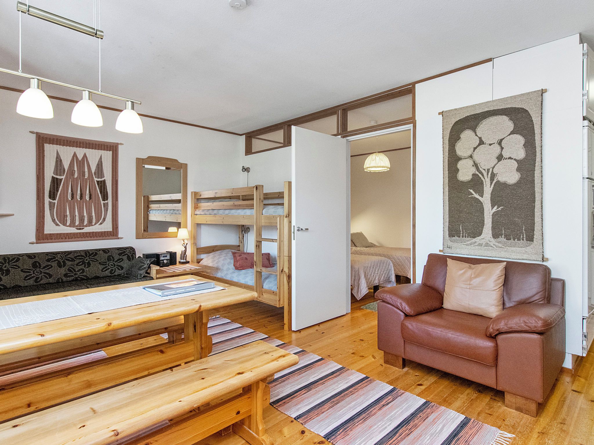 A cozy room with a wooden bench, a brown leather sofa, a bed with a wooden headboard, and a wall-mounted mirror.