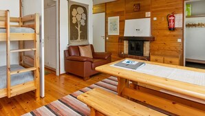 Una habitación acogedora con una cama nido de madera, un sofá de cuero marrón, una mesa de comedor de madera con bancos, una chimenea y un candelabro.