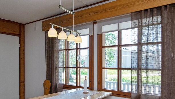 Una habitación con una mesa de madera, bancos y una ventana con cortinas.