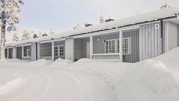 A row of cabins with large windows and a covered porch, surrounded by snow.