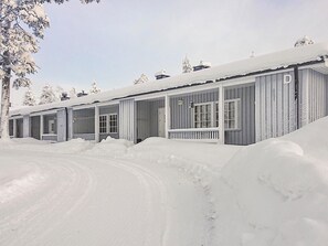Una hilera de cabañas con ventanas amplias y un porche cubierto, rodeadas de nieve.