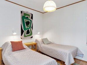 Una habitación con dos camas individuales, una mesita de noche de madera, una obra de arte abstracta colgada en la pared y una lámpara en el techo.