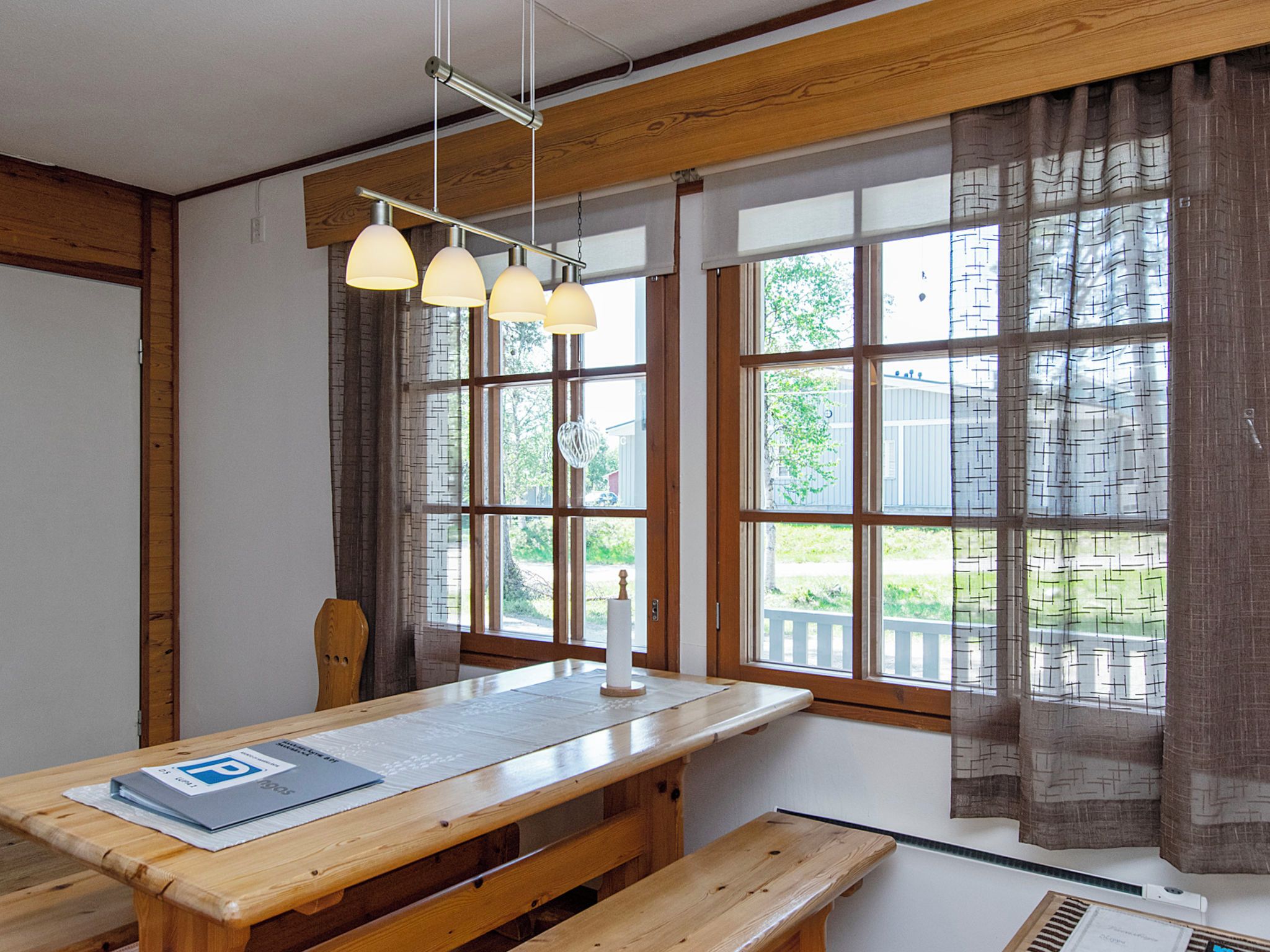 A room with a wooden table, benches, and a hanging light fixture.