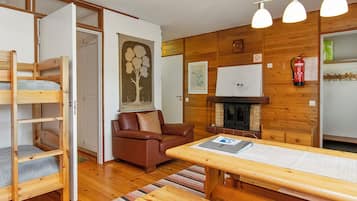 A cozy room with a wooden bunk bed, a brown leather sofa, a wooden dining table, and a fireplace.