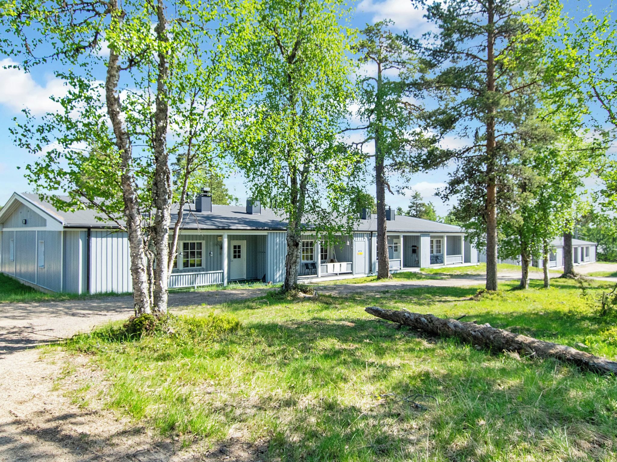 A row of single-story houses with a porch, surrounded by trees and grass.