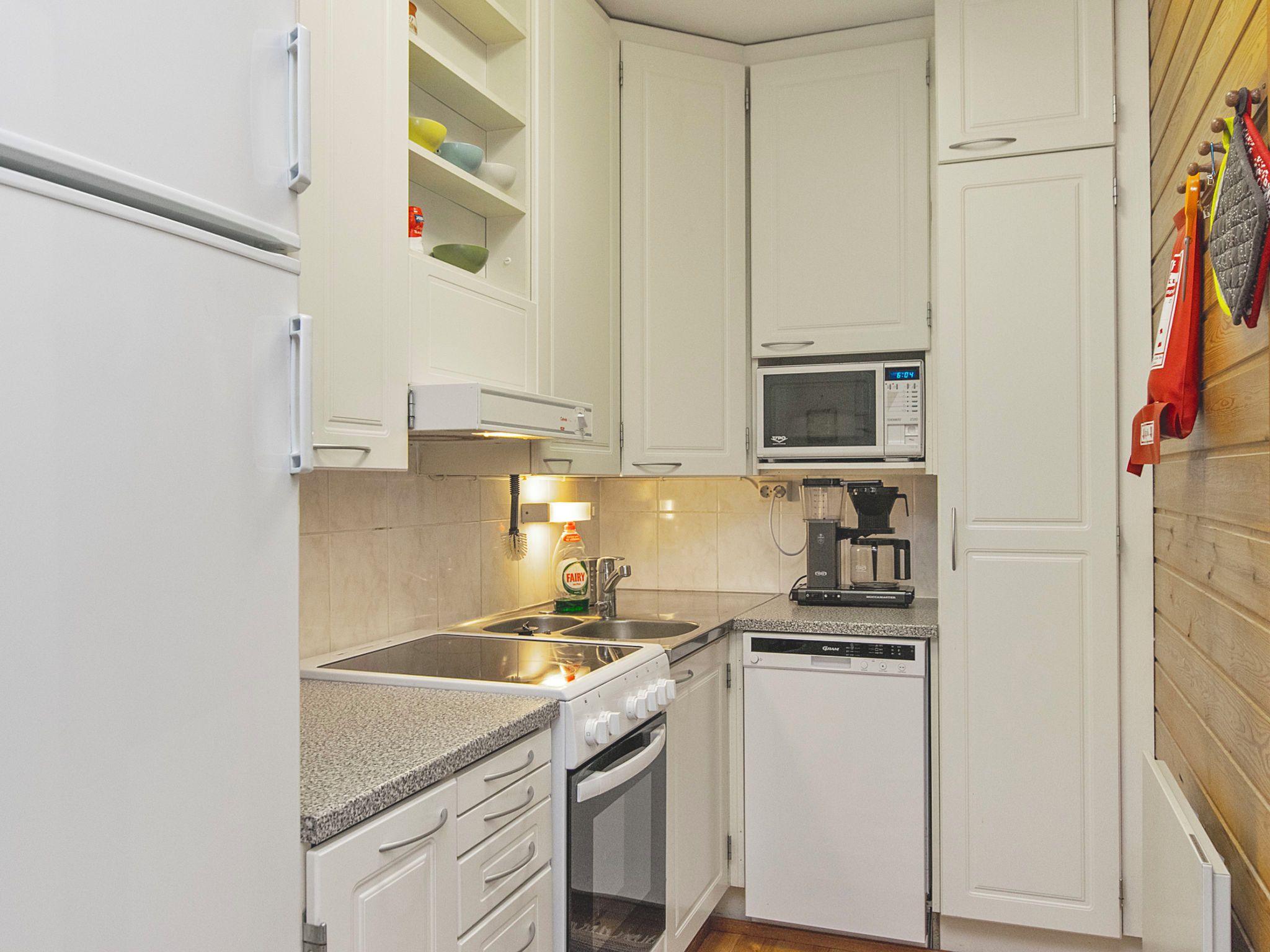 A compact kitchen with white cabinets, a microwave, a coffee maker, and a dishwasher.